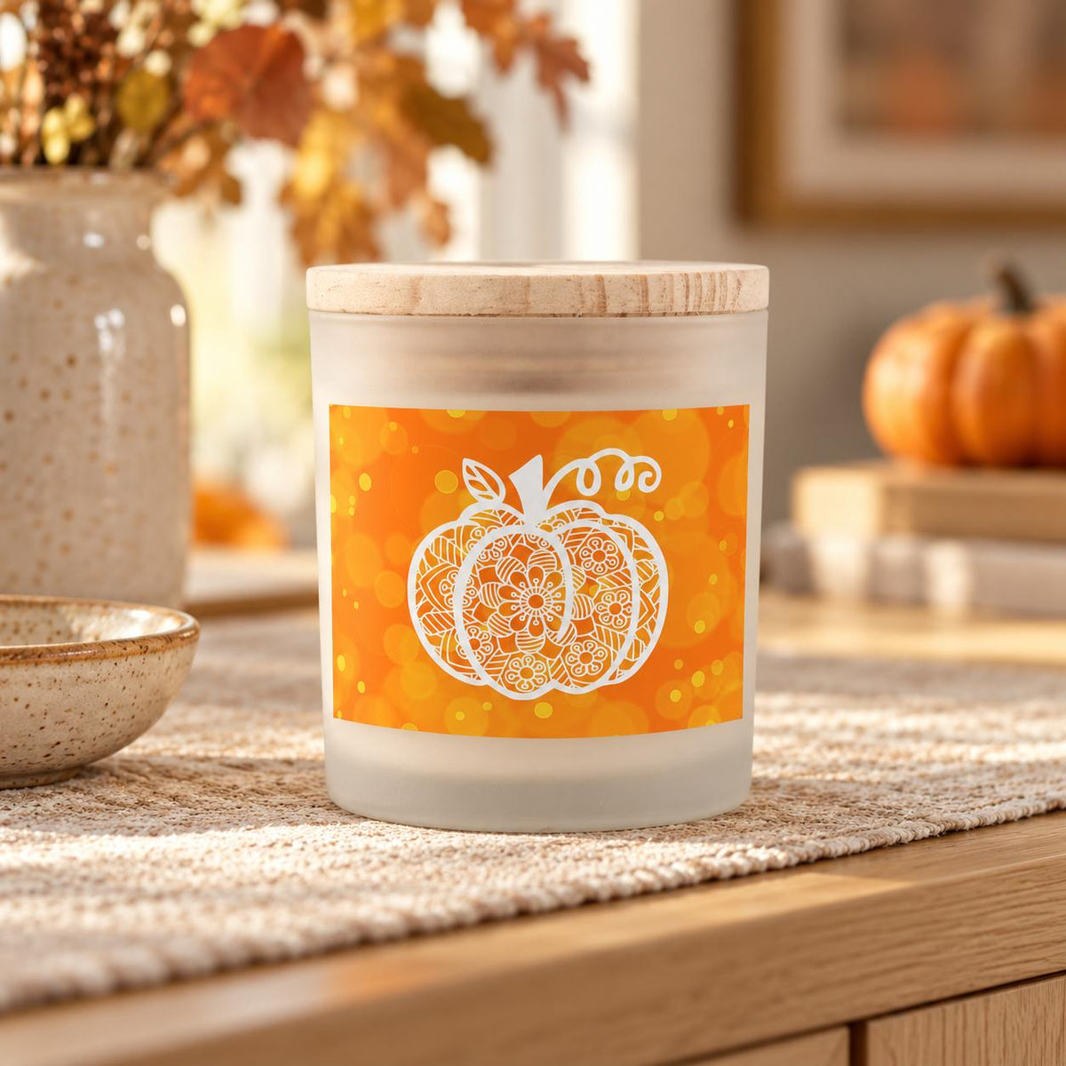 White mandala pumpkin candle with orange bokeh label and wooden lid on an autumn sideboard